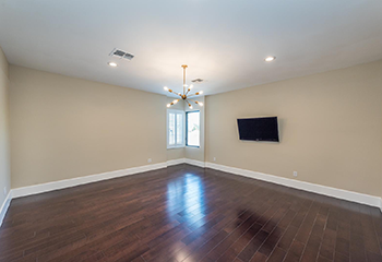 The image shows a newly remodeled living room with dark wood flooring, beige walls, and modern recessed lighting.